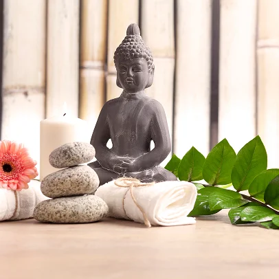 Statue de Bouddha, pierres zen, bougie, serviettes blanches et fleur rose.