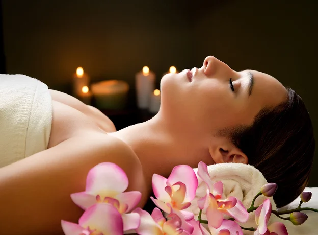 Femme détendue sur une table de massage, entourée de bougies et d'orchidées roses à Lucé près de Chartres en Eure-et-Loir 28