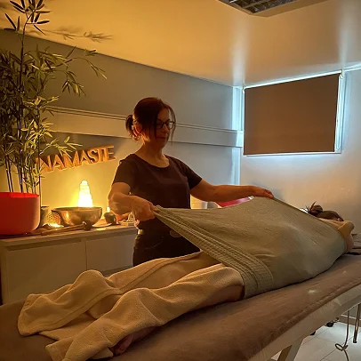 Thérapeute couvrant une personne allongée sur une table de massage dans une pièce éclairée.